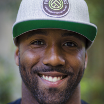 a person looking straight at the camera, smiling with a grey and green baseball style cap on